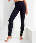 A person wearing high-waisted black Tri-Dri TR039 leggings is standing barefoot against a white background with one arm resting on a surface. Only the lower half of the body is visible.