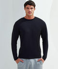 A man wearing a long-sleeve black Tri-Dri TR050 shirt and gray sweatpants stands against a plain background with his hands in his pockets, looking directly at the camera.