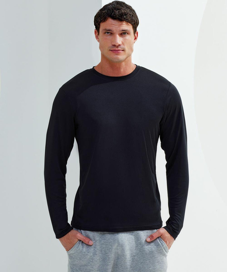 A man wearing a long-sleeve black Tri-Dri TR050 shirt and gray sweatpants stands against a plain background with his hands in his pockets, looking directly at the camera.