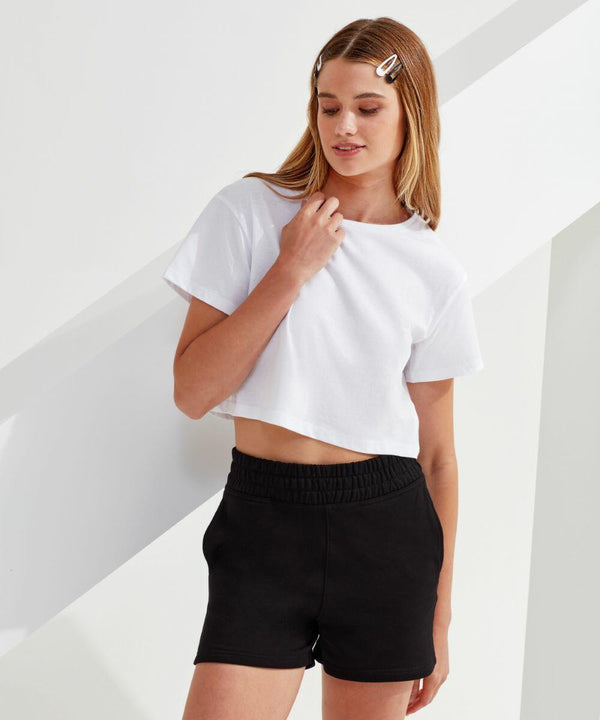 A person with long hair stands against a white background, wearing a white TR062 T-shirt by TriDri and black shorts, with hair clips on the left side of their head.