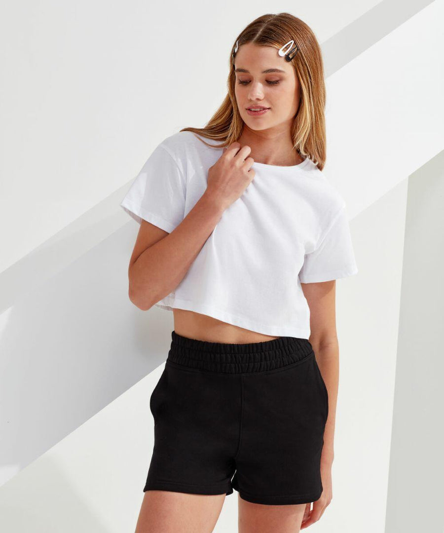 A person with long hair stands against a white background, wearing a white TR062 T-shirt by TriDri and black shorts, with hair clips on the left side of their head.