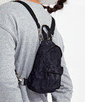 Person wearing a gray sweater with a small black Tri-Dri TR094 backpack over one shoulder, positioned diagonally across their back.