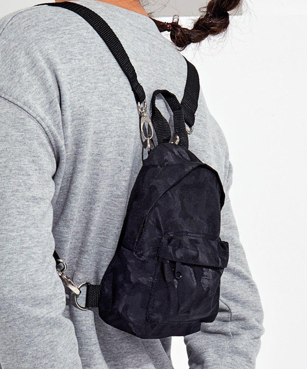 Person wearing a gray sweater with a small black Tri-Dri TR094 backpack over one shoulder, positioned diagonally across their back.