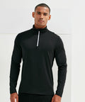 A man stands wearing a black, long-sleeve, zip-up top, looking directly at the camera. The background is plain and white. He is dressed in the Tri-Dri TR111.