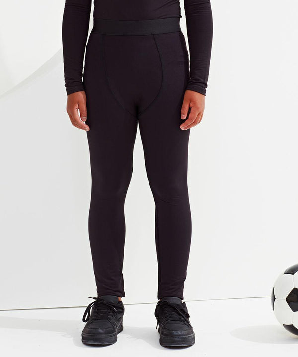 A person wearing black Tri-Dri TR17B athletic leggings and black sports shoes, standing next to a soccer ball.