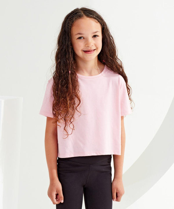 A young girl with long curly hair stands smiling while wearing a light pink Tri-Dri TR19B t-shirt and black pants.