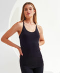 A woman with long hair stands against a light-colored background, wearing a black Tri-Dri TR217 ribbed tank top and black leggings.