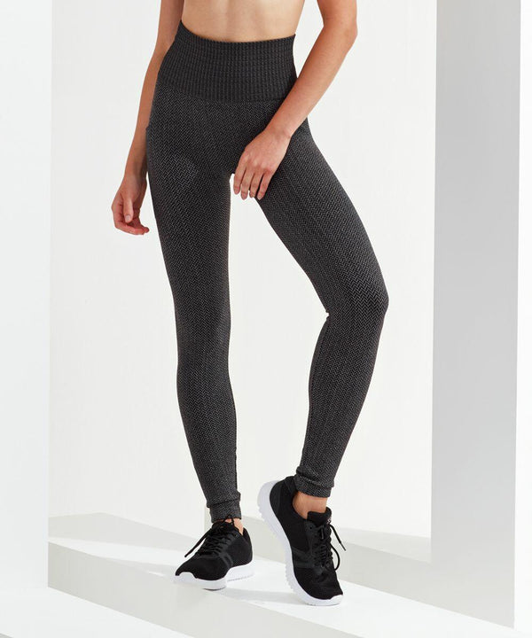 A person wearing dark grey, high-waisted Tri-Dri TR219 leggings and black athletic shoes stands against a white background. Their upper body is not visible.