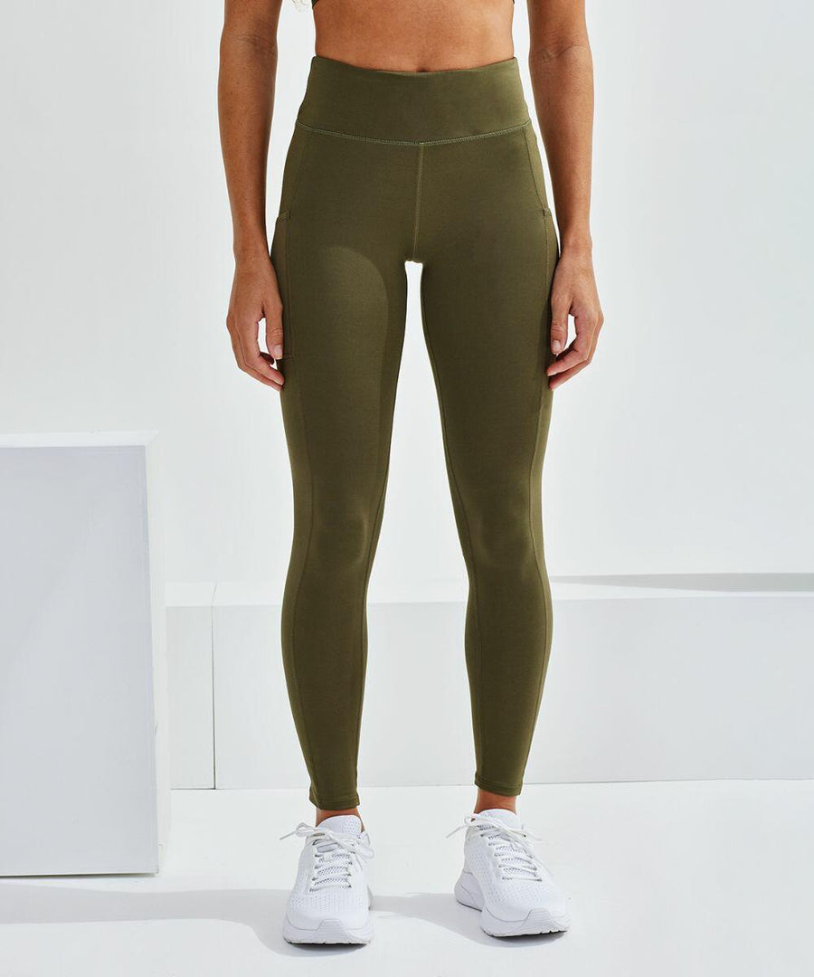 A person stands against a white background, wearing olive green TR304 leggings from Tri-Dri and white sneakers. The top half of their body is not visible.