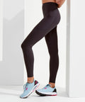 A person wearing black high-waisted leggings and light blue Tri-Dri TR308 running shoes with black and pink details stands against a white background.