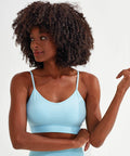 A person with curly hair is wearing a light blue Tri-Dri TR510 sports bra and looking to the right, against a plain white background.