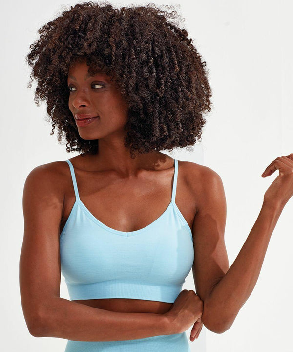 A person with curly hair is wearing a light blue Tri-Dri TR510 sports bra and looking to the right, against a plain white background.