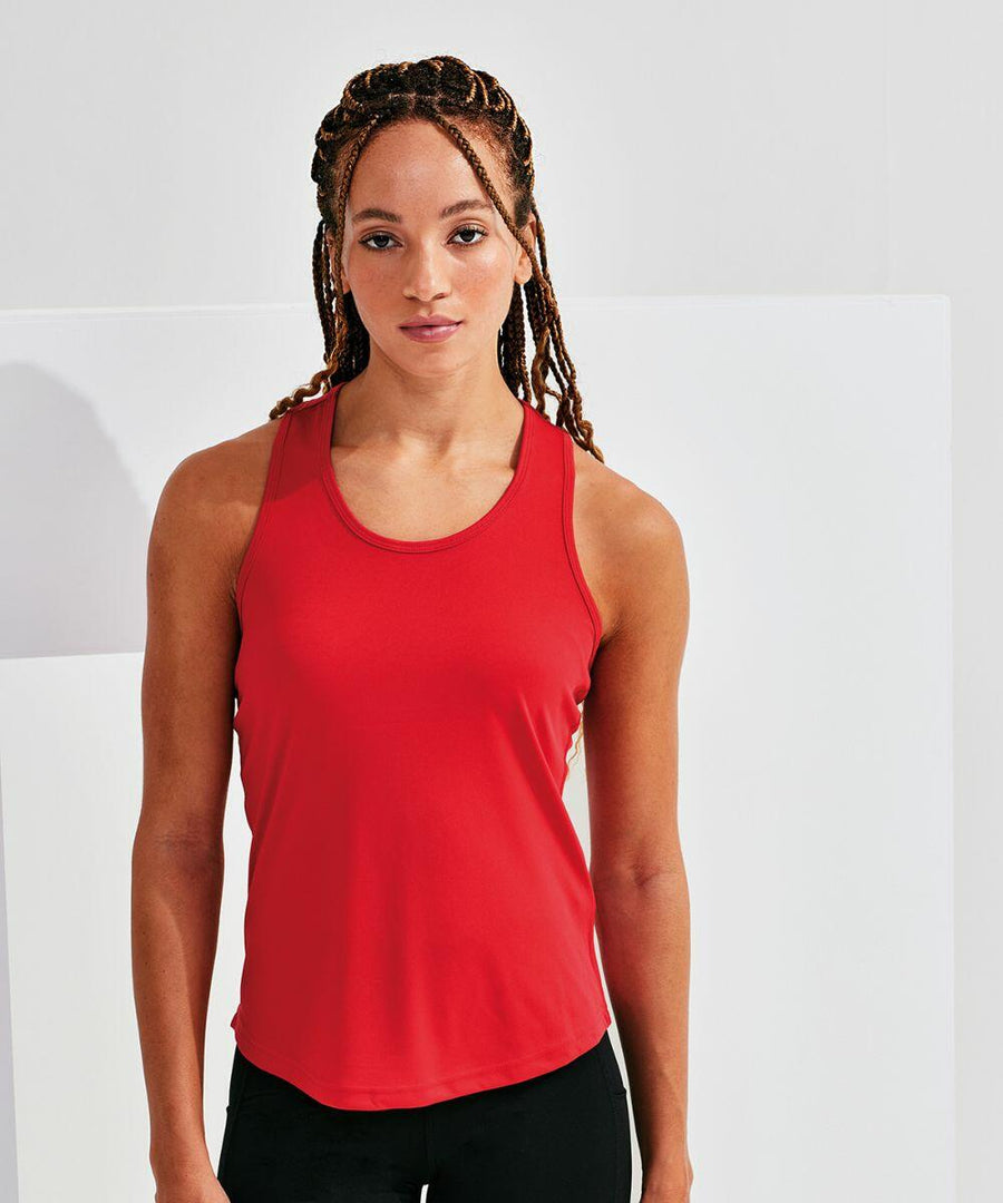 A woman with long braided hair wearing a red Tri-Dri TR527 sleeveless top and black pants stands against a white background.