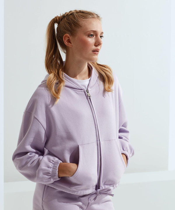 A person with blonde hair in a ponytail, wearing a light purple Tri-Dri TR601 zip-up hooded sweatshirt, stands with hands in pockets, looking to the side.