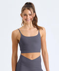 A young woman with long brown hair in a ponytail wears the TriDri Womens TriDri recycled Luxe bra and smiles whilst standing in front of a plain light background.