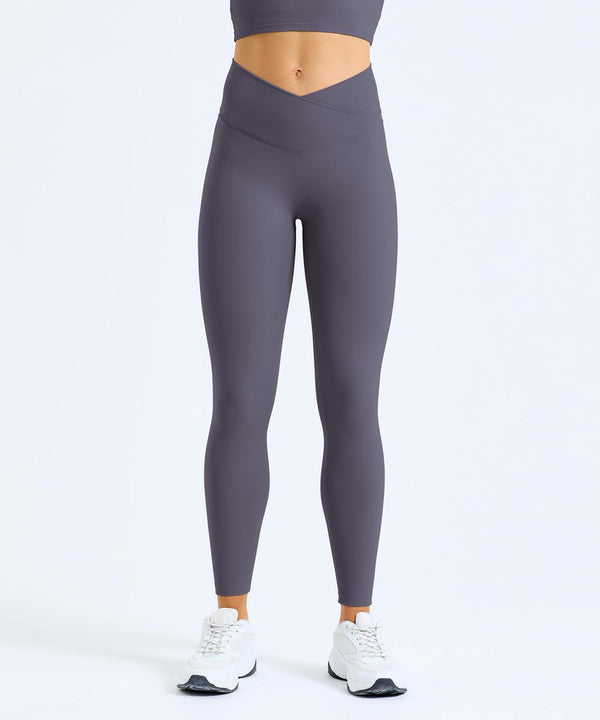 Only the lower torso and legs are visible as a person stands against a plain white background, wearing TriDri Women's TriDri recycled Luxe leggings in greyish-purple with white trainers.