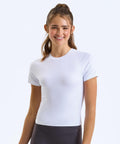 A young woman with long brown hair in a ponytail smiles whilst wearing the TriDri Women’s TriDri recycled Luxe fitted tee in white and black leggings, standing against a plain white background.