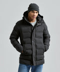 A person wears the 2786 Recycled Bonded Longline Padded Jacket in dark grey, paired with a grey knit beanie and blue jeans, standing with hands in jacket pockets against a plain light grey background.