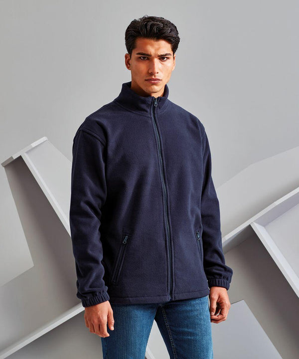 A person stands against a neutral backdrop wearing a dark blue TS014 zip-up jacket by 2786 with hands in the pockets and blue jeans.