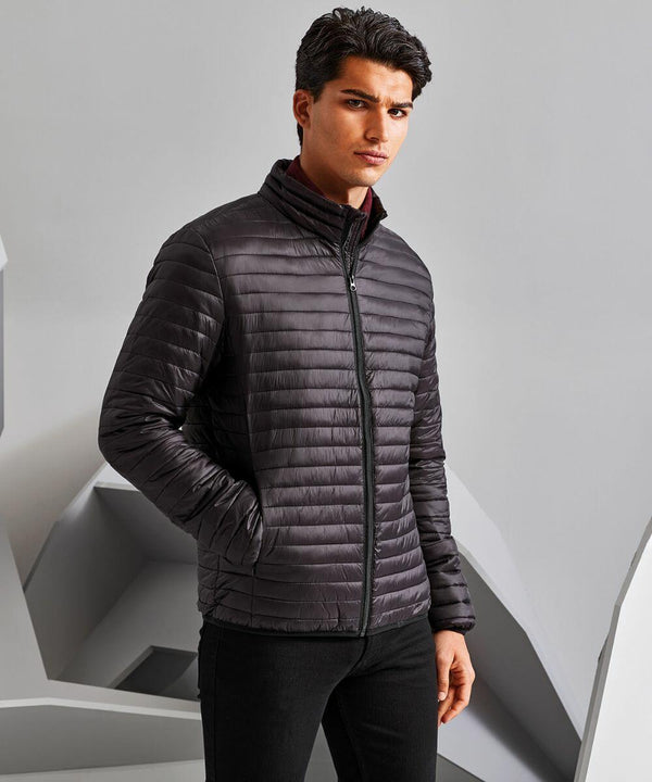 A man stands wearing a dark, quilted TS018 jacket with a zipper in front by 2786, posing against a grey background.
