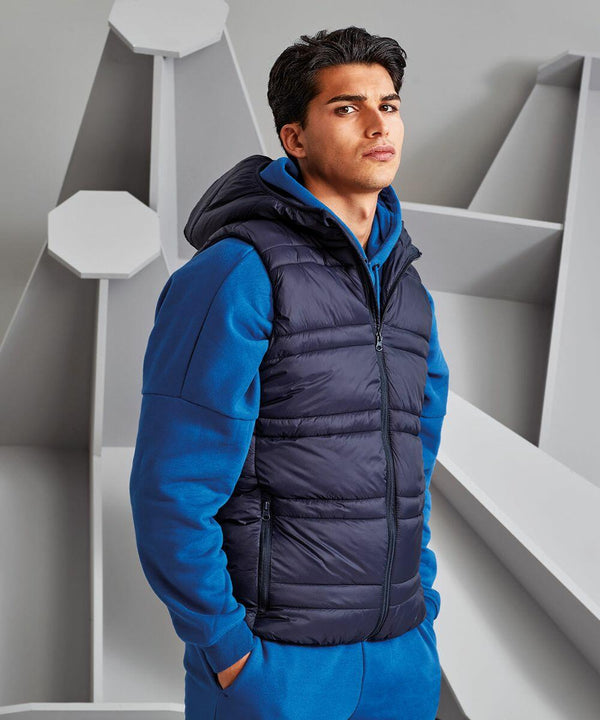A man in a blue hoodie and a black 2786 TS039 stands indoors, gazing into the camera with a neutral expression.