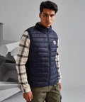 A man wearing a navy 2786 TS040 vest over a plaid shirt stands indoors with a neutral expression. He has short dark hair and is looking directly at the camera.