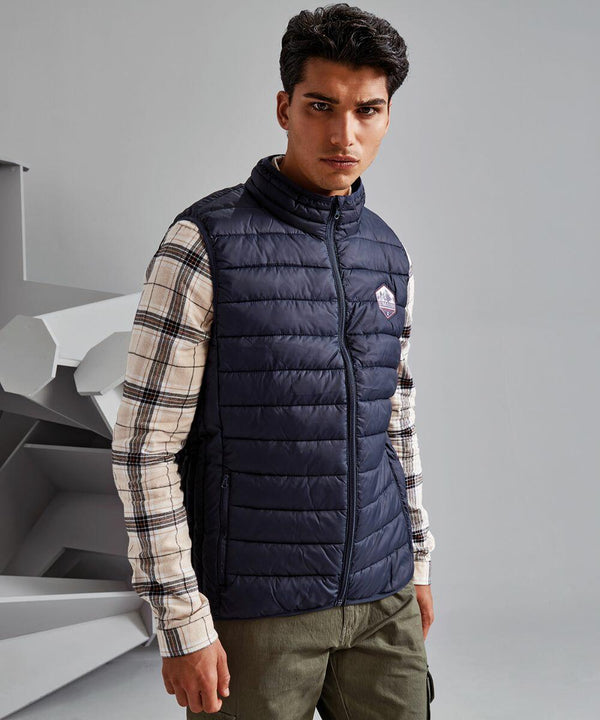 A man wearing a navy 2786 TS040 vest over a plaid shirt stands indoors with a neutral expression. He has short dark hair and is looking directly at the camera.