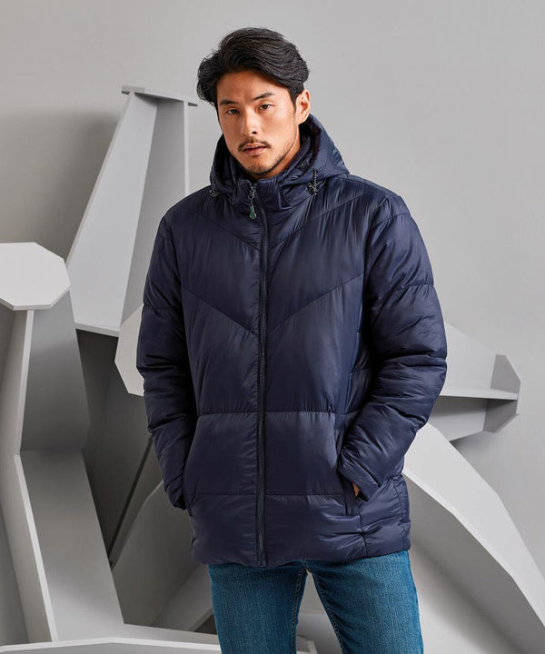 A man in a dark blue TS045 puffer jacket by 2786 with his hands in the pockets stands against a backdrop with geometric shapes.