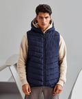 A person stands against a plain background wearing a navy blue 2786 TS047 puffer vest over a beige hoodie and grey pants.