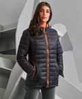A person stands against a geometric backdrop, wearing a dark quilted jacket with orange accents from the 2786 brand, product name TS16F.
