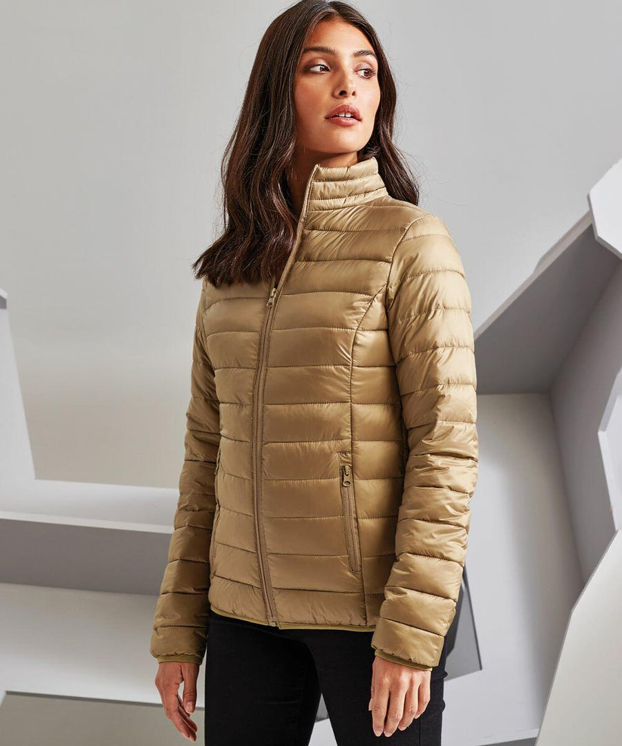 A person with long brown hair is wearing a tan 2786 TS30F and black pants, standing against a geometric background.