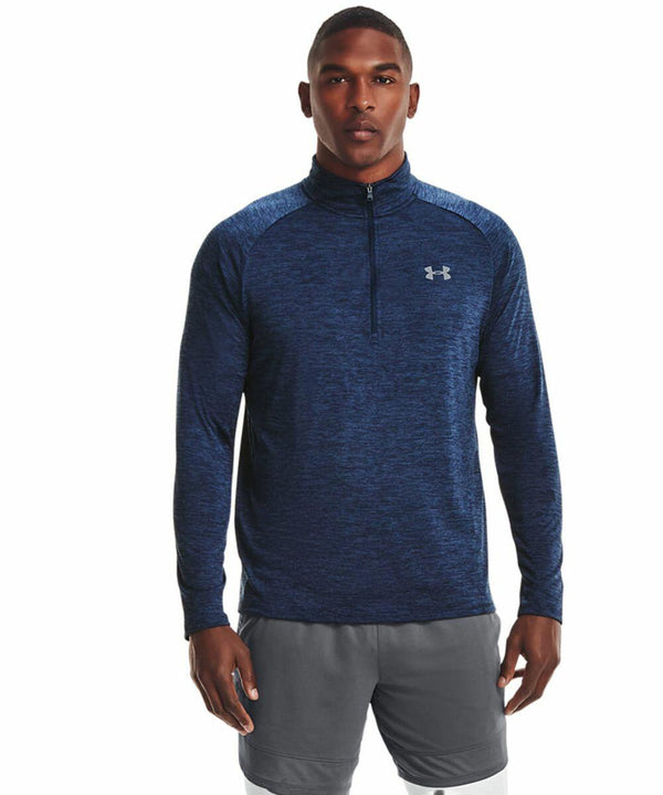 A man is wearing a navy blue, long-sleeve athletic pullover with a quarter-zip and the Under Armour logo on the chest, named UA004 by Under Armour, paired with gray shorts.