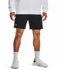 Man wearing a white long-sleeve shirt, black athletic shorts with a small Under Armour logo, white socks, and white Under Armour UA050 sneakers stands against a plain background.