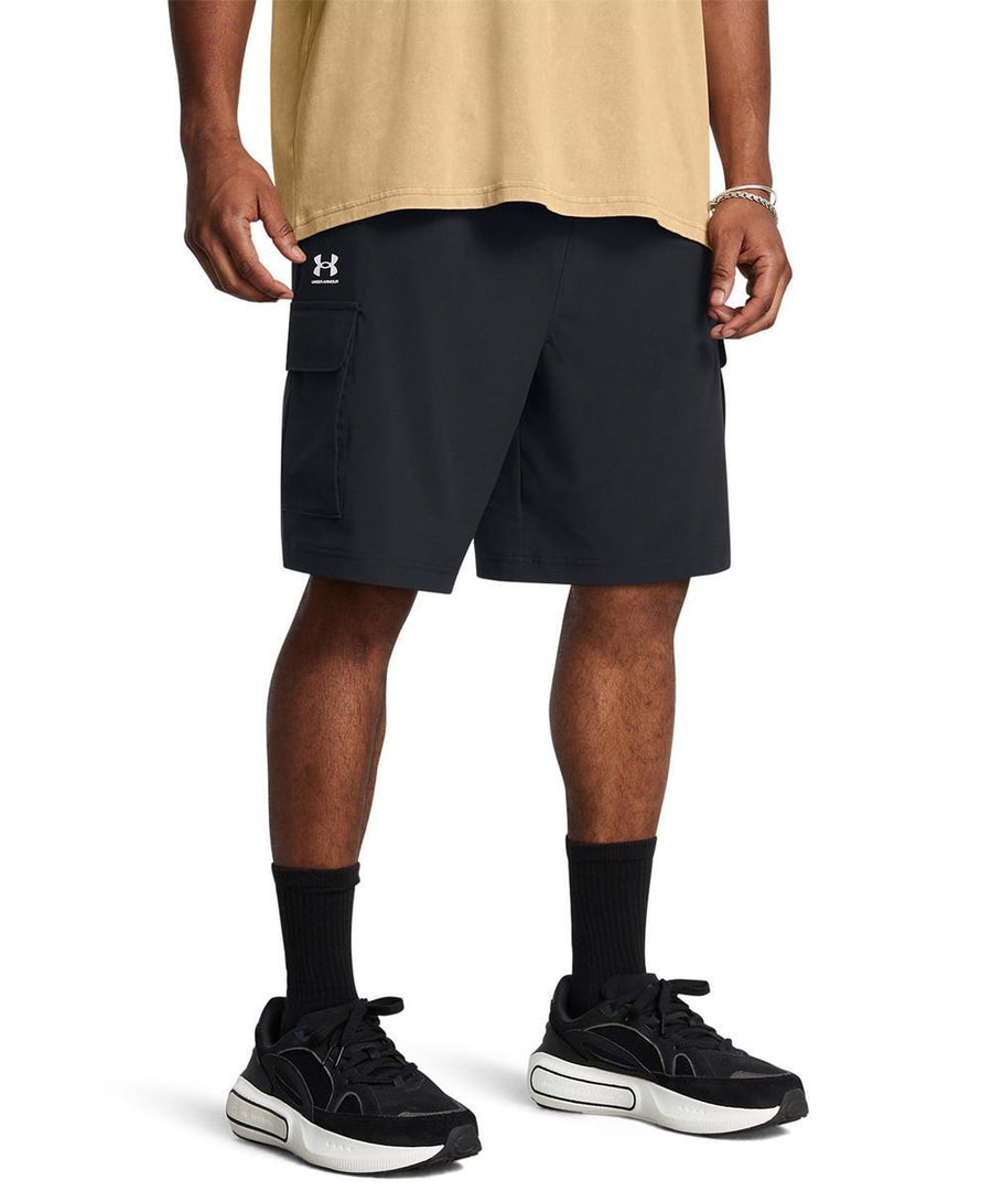 A person wearing a beige T-shirt, Under Armour UA Vibe cargo shorts in black, black crew socks, and black and white trainers stands against a plain white background.