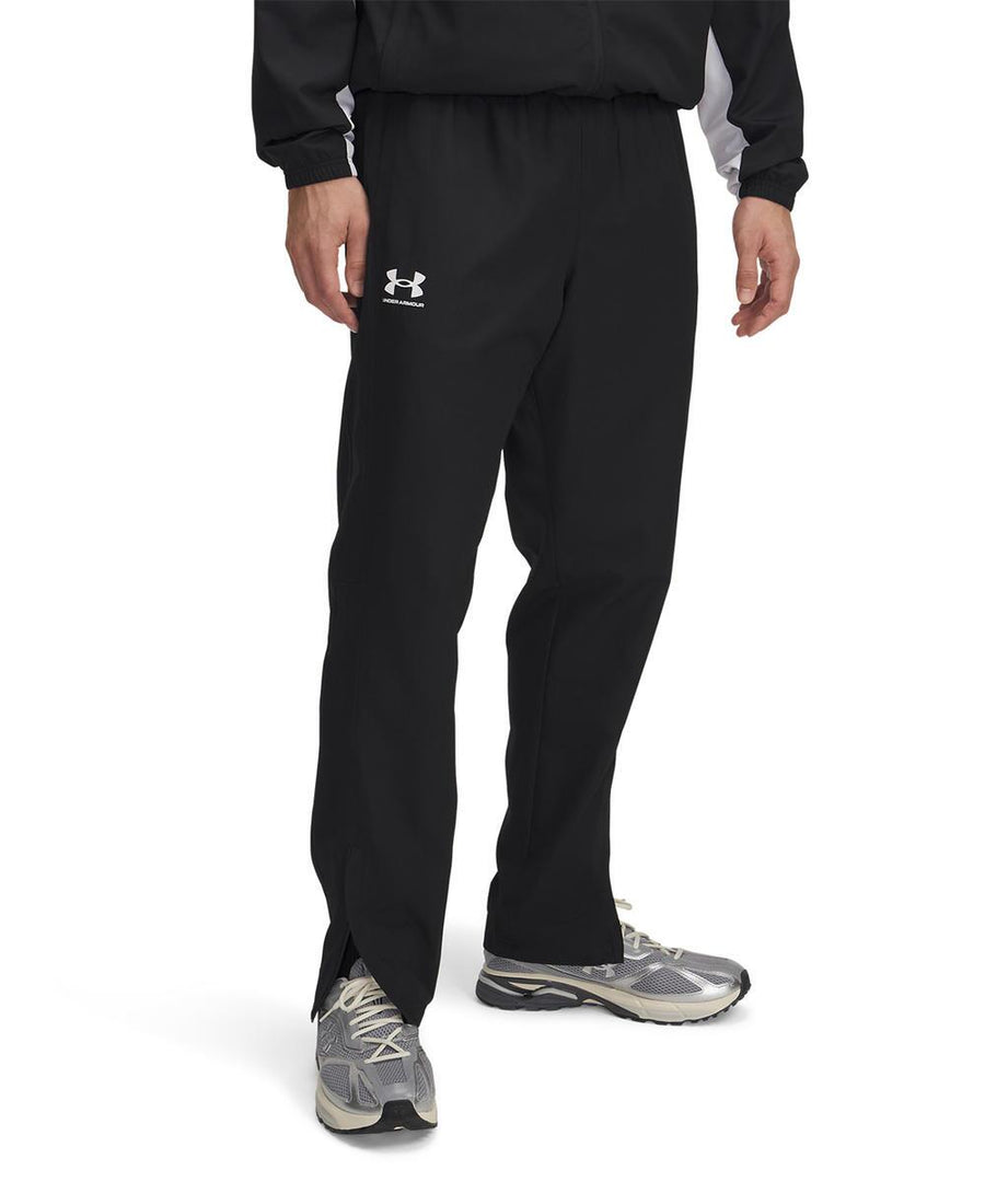 A person wearing Under Armour UA Rival woven windbreaker trousers stands against a plain white background, with only their lower half visible.