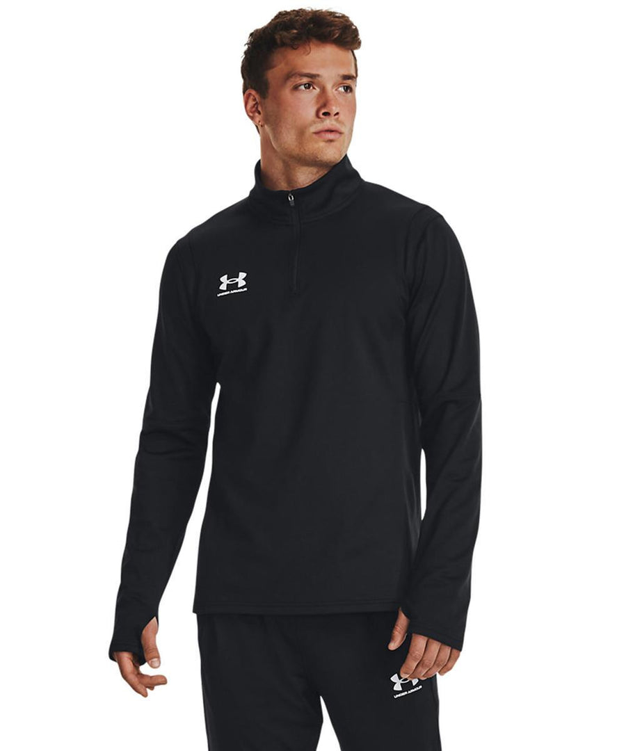 A man stands facing slightly right, wearing a black Under Armour UA Challenger 1/4-zip pullover and matching black trousers, both featuring the Under Armour logo. His left hand hangs relaxed at his side.