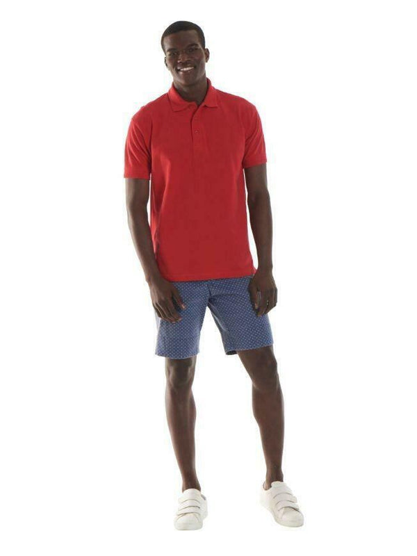 A man wearing a UC104 Red Uneek ultimate pique polo shirt with Blue shorts