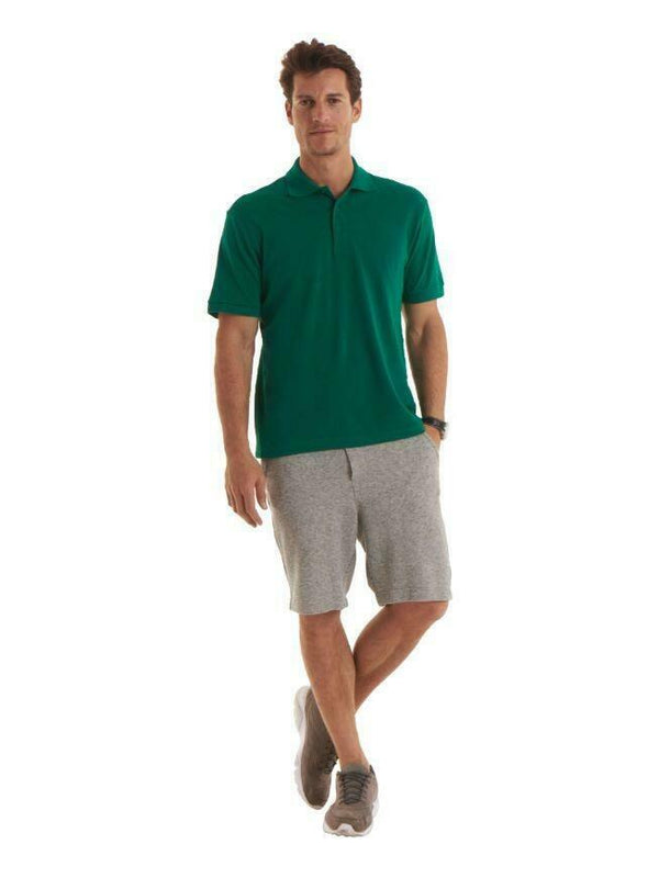 A man wearing a UC114 Kelly Green Uneek mens ultra cotton polo shirt with Beige Shorts