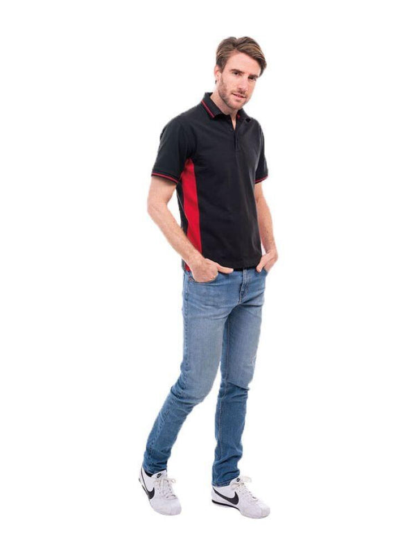 A man wearing a UC117 Black and Red Uneek two tone polo shirt with blue jeans and white trainers