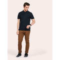 A man wearing a UC127 Black Uneek mens super cool workwear polo shirt with Brown trousers