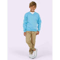 A boy wearing a UC206  Uneek Sky childrens v-neck sweatshirt with Beige trousers