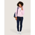 A woman wearing a UC505 Pink Uneek ladies classic full zip hoodie with Blue jeans