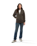 A woman wearing a Uneek UC203 unisex deluxe sweat jacket in Charcoal with blue jeans and white trainers