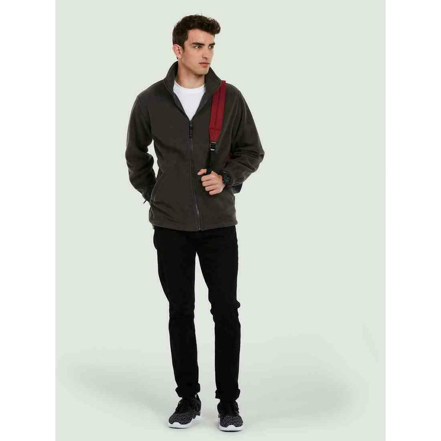 A man wearing a UC601 Charcoal Uneek adults heavyweight full zip fleece with Black jeans