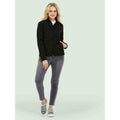 A woman wearing a UC613 Black Uneek ladies classic soft shell jacket with Grey jeans