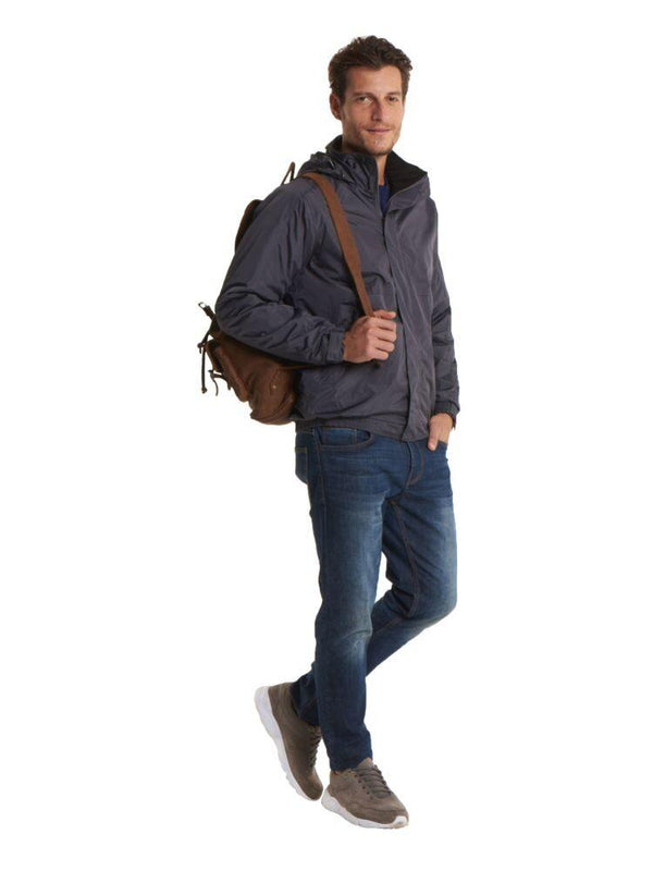 A Man wearing a Uneek Premium Outdoor Jacket in Deep Grey & Black and blue jeans on a white background