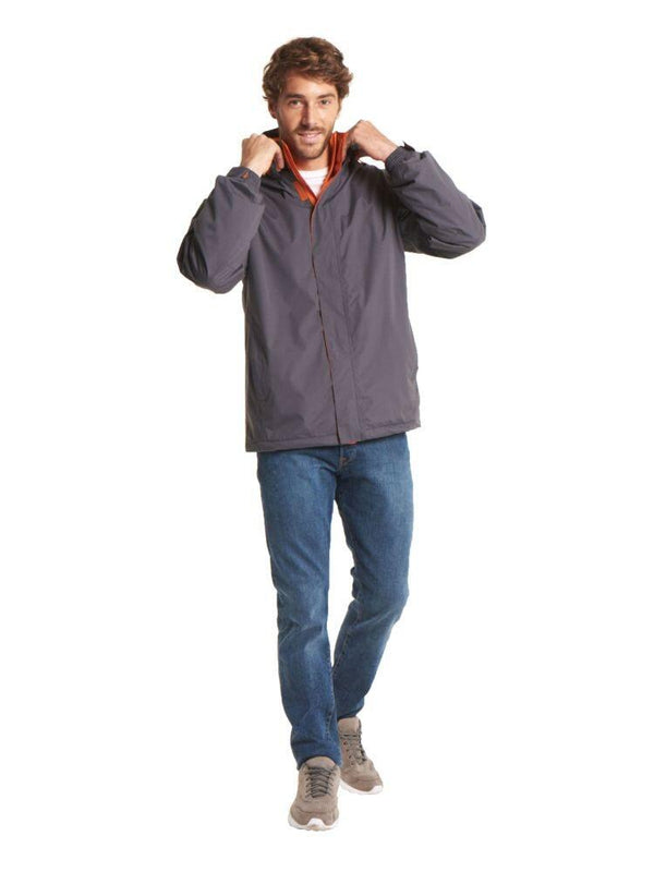 A man wearing a Uneek UC621 Deluxe Outdoor Jacket in Deep Grey & Fiery Orange and blue jeans on a white background