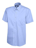 UC702 Mid Blue button-up short-sleeved shirt by Uneek displayed on a white background, featuring a pointed collar and a left chest pocket.