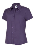 A purple, button-up shirt with short sleeves and a pointed collar from Uneek (UC712), displayed on a plain white background.