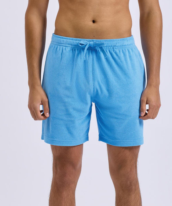 A person wearing Wombat Men's Terry shorts in light blue stands against a plain light background. The photo captures them from mid-torso to just above the knees.